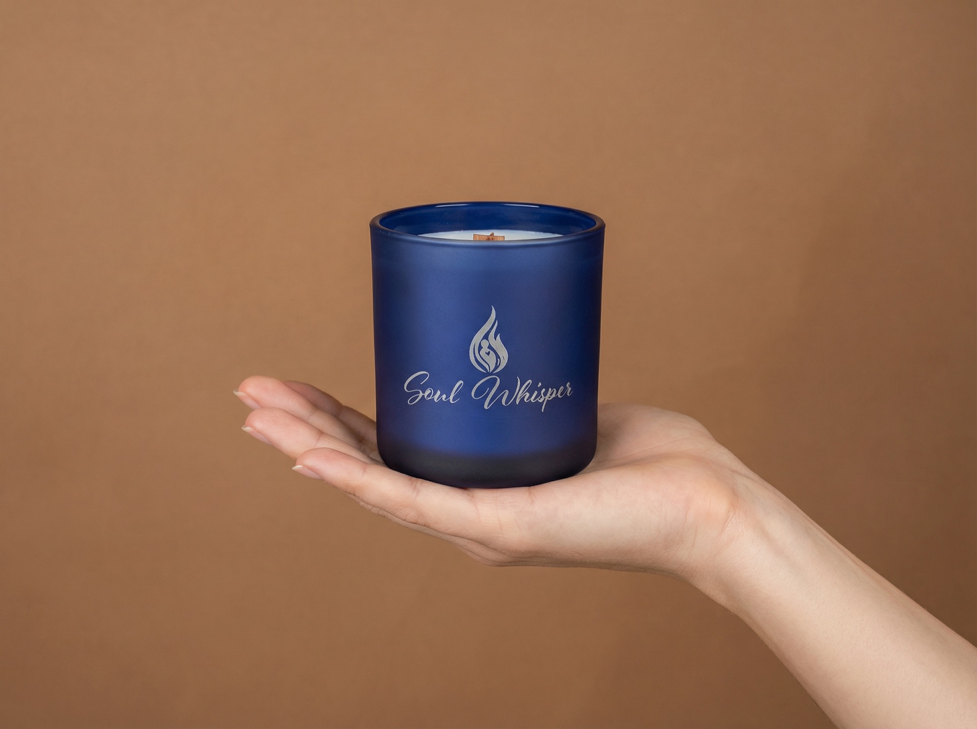 Hand holding a Soul Whisper blue candle against a warm brown background